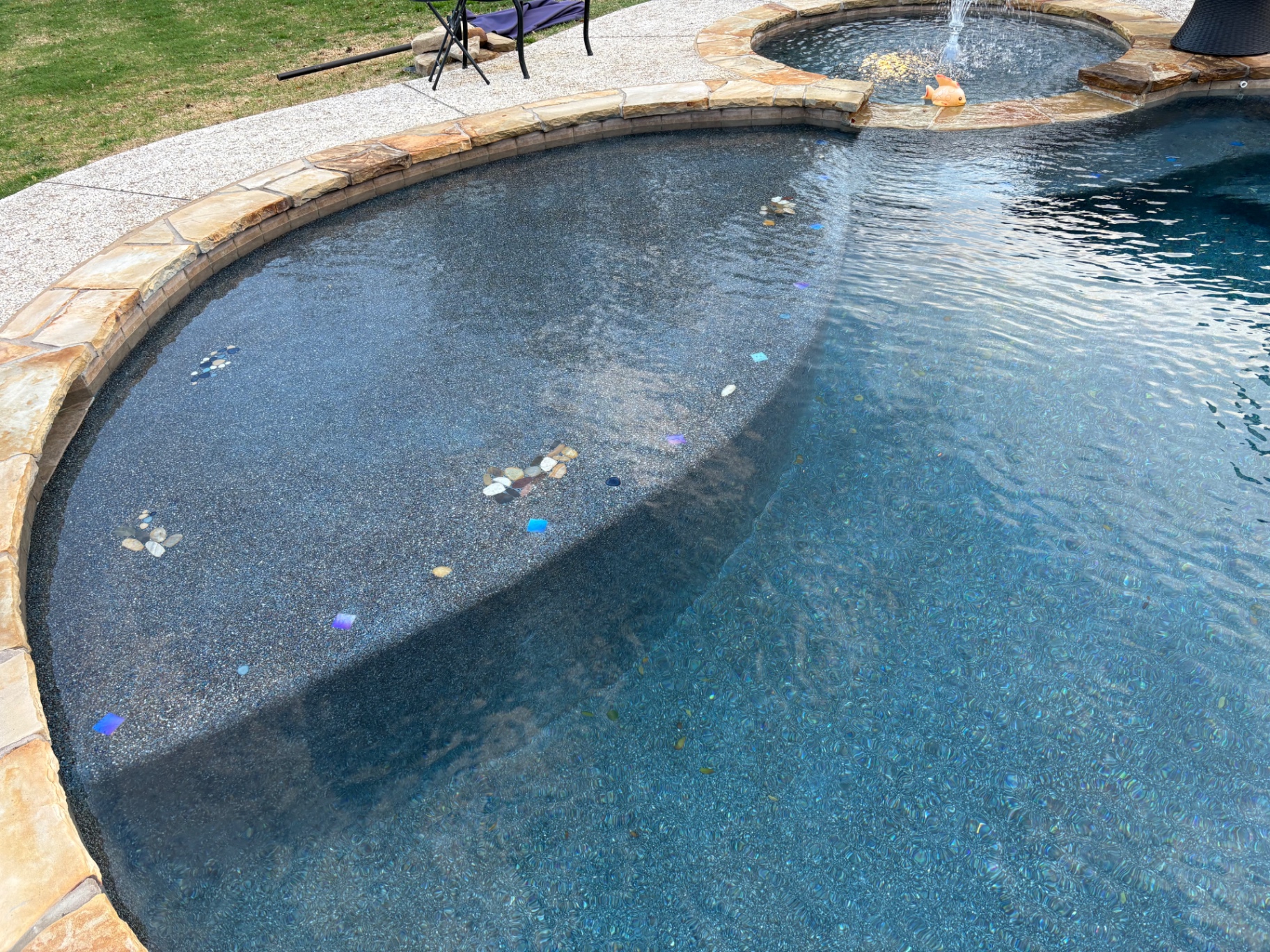 Freeform pool with dark pebble finish, flagstone coping, and pebble and glass tile step accents