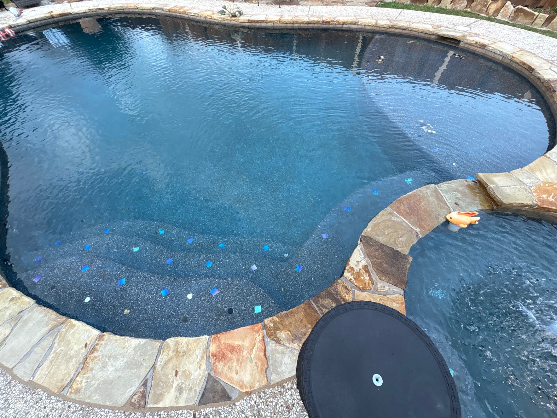 Dark pebble freeform pool and attached spa with flagstone coping and iridescent glass tile step accents