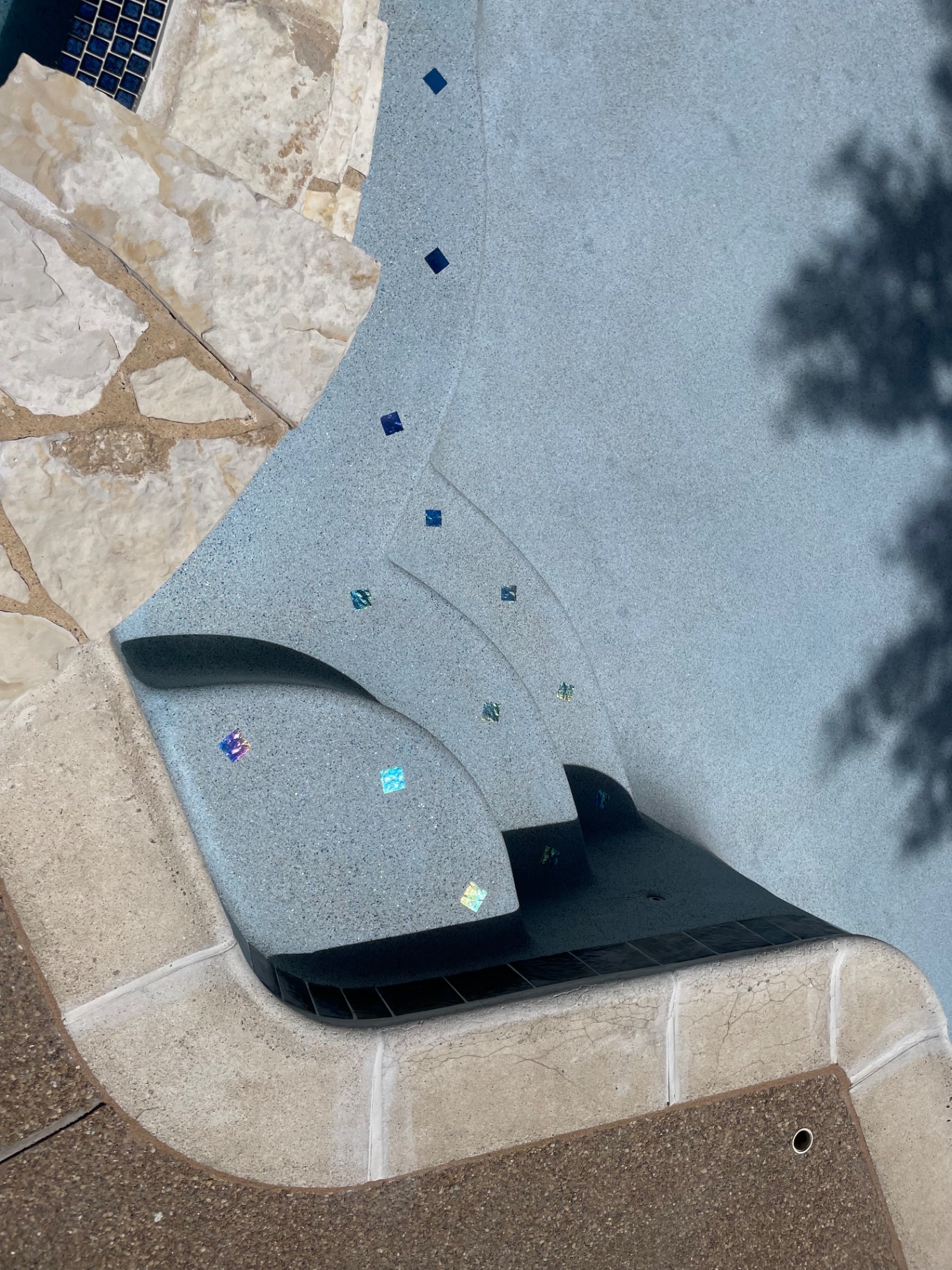 Close-up of pool entry steps with iridescent glass tile accents and limestone coping