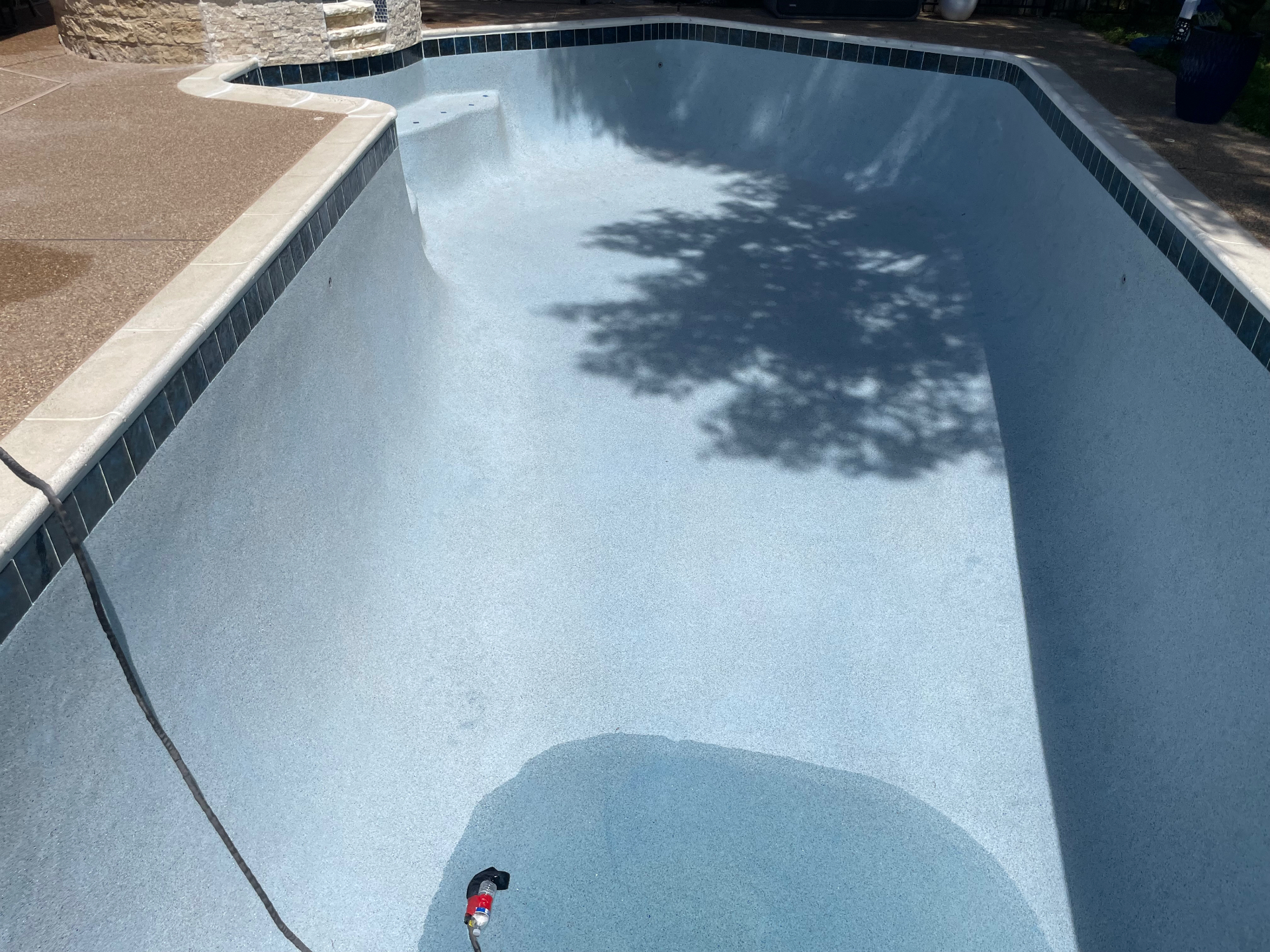 Freshly resurfaced geometric pool with blue waterline tile and tanning ledge
