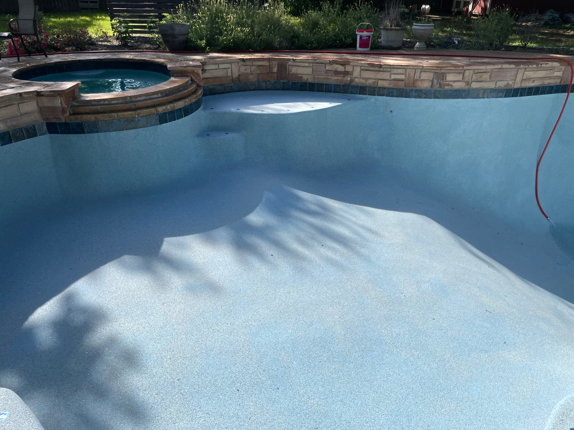 Freeform pool with attached spa, stacked stone wall, and blue waterline tile filling with water