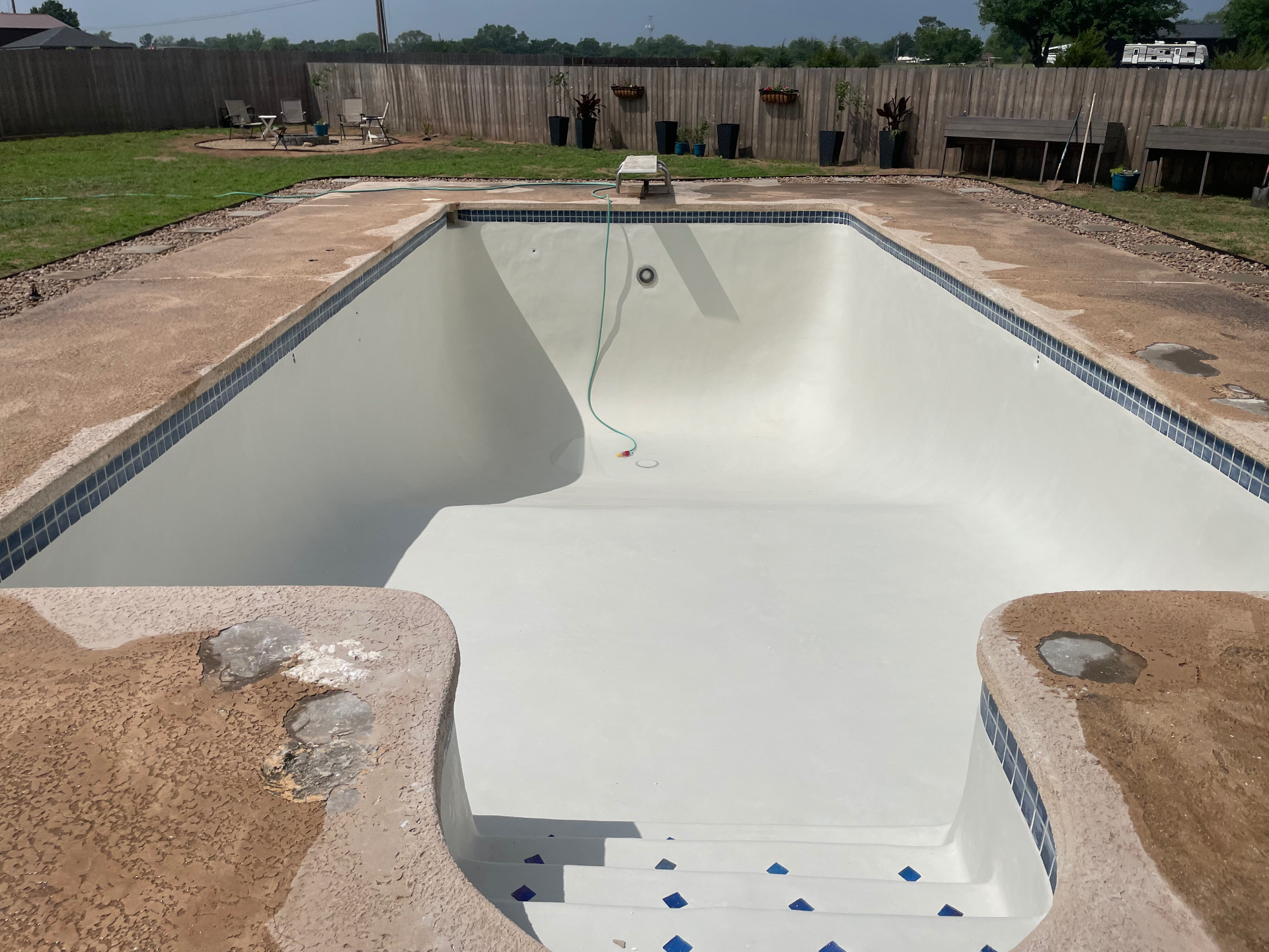 Rectangular pool with fresh white plaster, blue waterline tile, and diving board