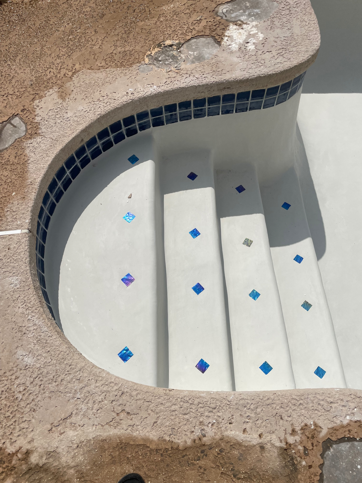 Close-up of pool entry steps with white plaster and iridescent blue glass tile accents
