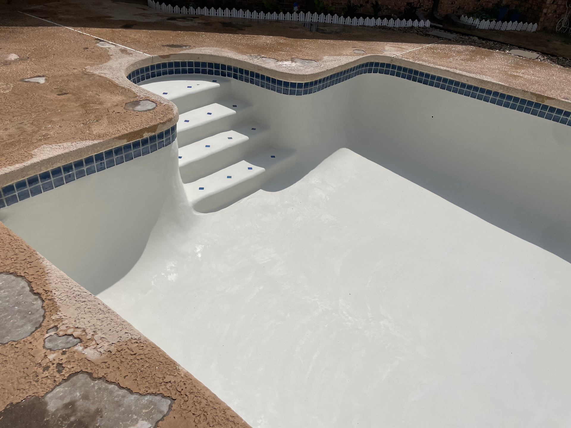Freshly resurfaced rectangular pool with white plaster, blue waterline tile, and step accents