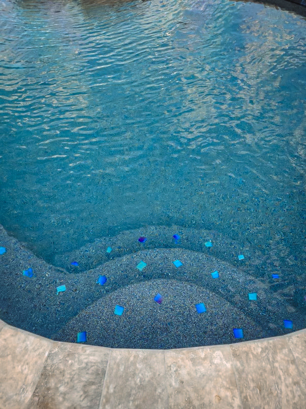 Pebble pool steps with blue glass tile accents underwater