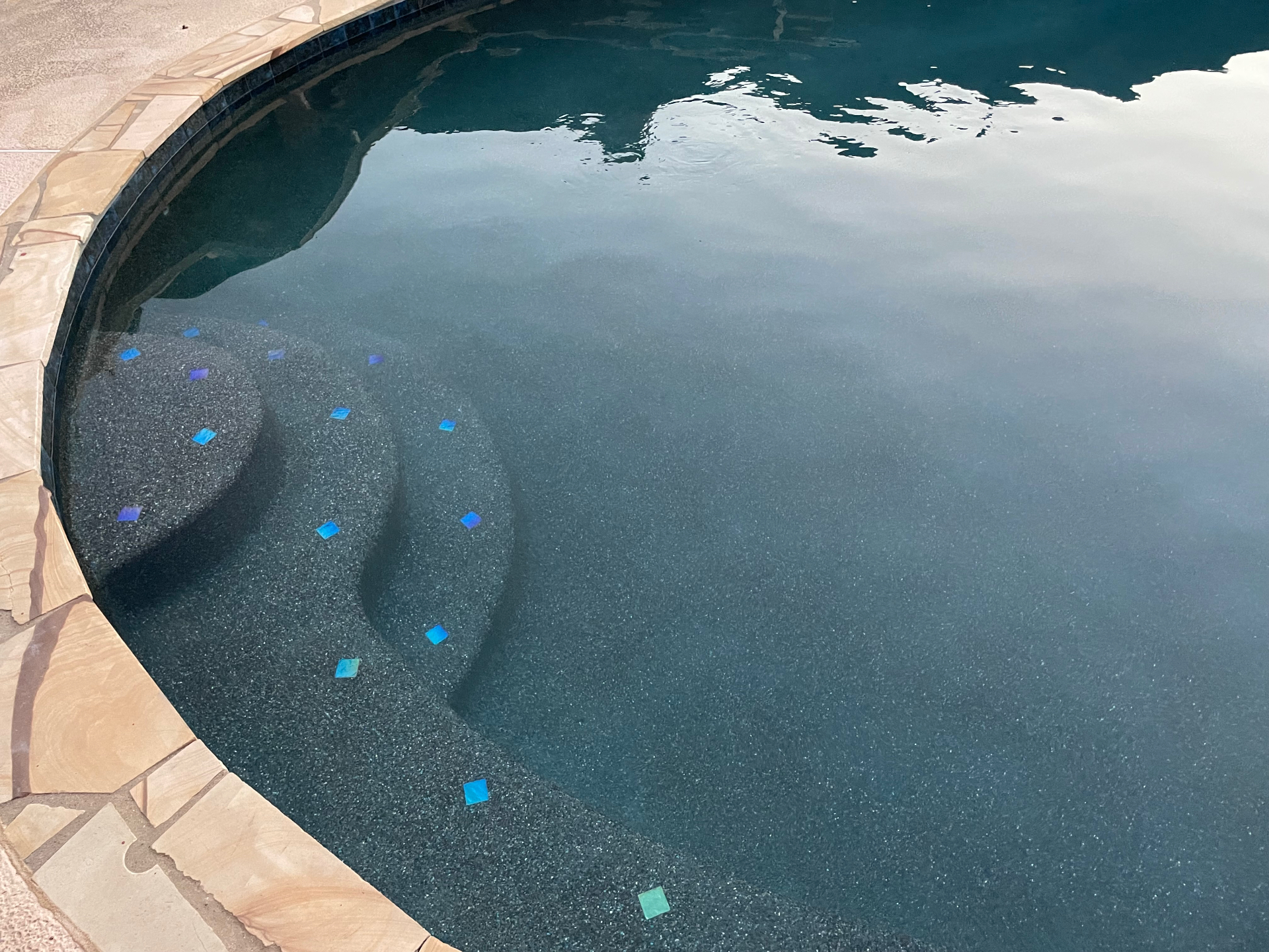 Dark pebble pool steps with iridescent blue glass tile accents and flagstone coping