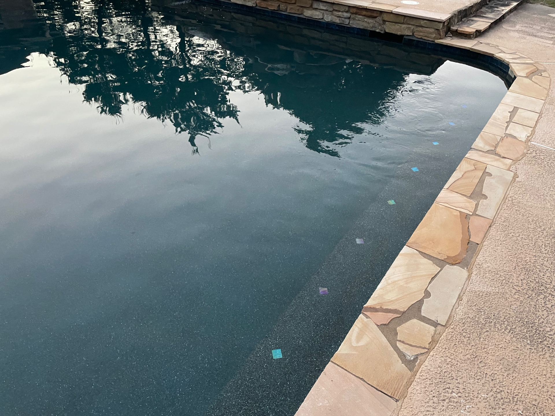 Dark pebble pool waterline with stacked stone wall and flagstone coping