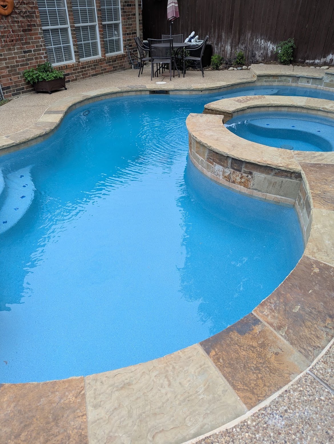 Freeform pool and attached spa with stacked stone wall and flagstone coping