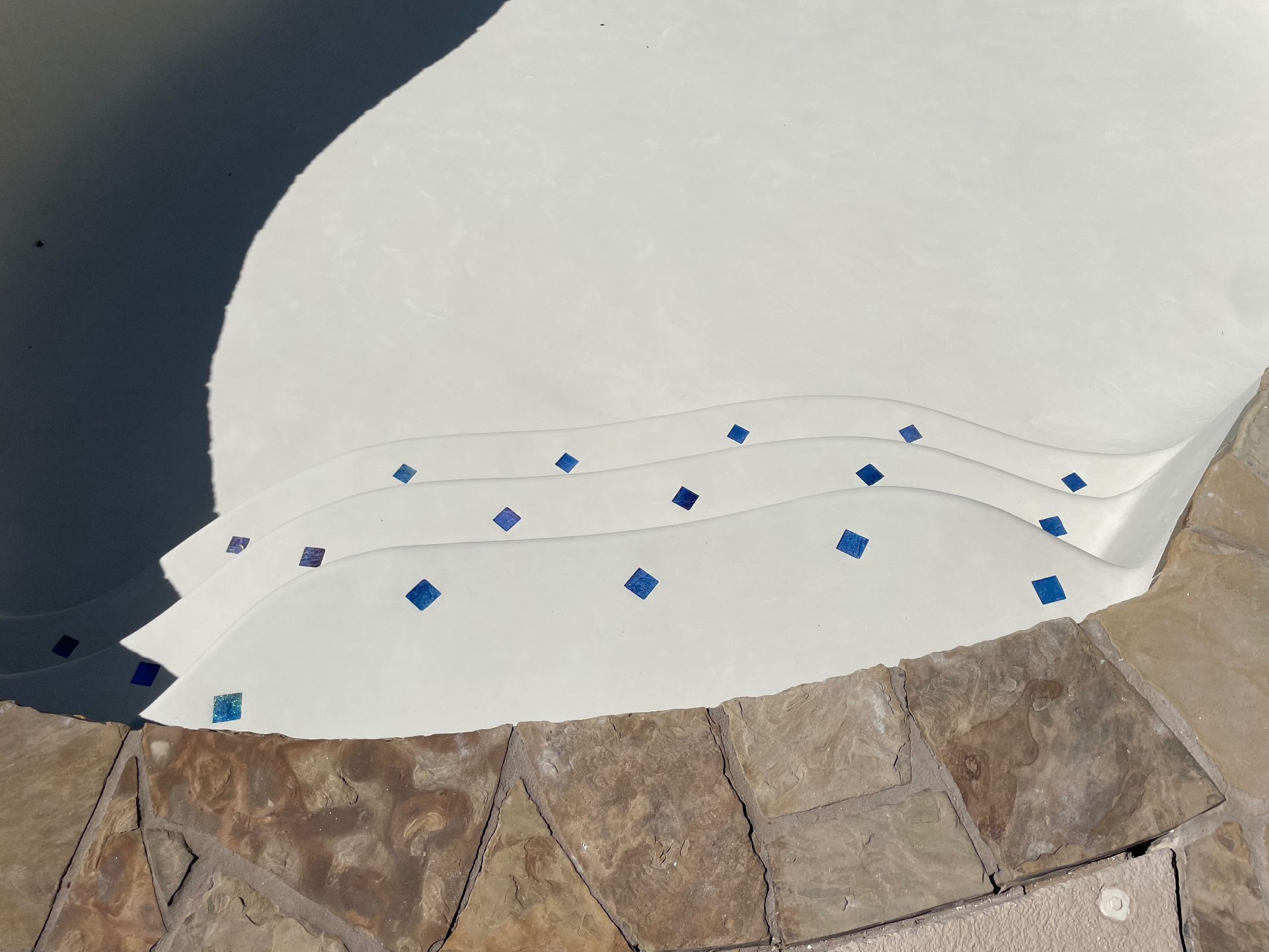 White plaster pool steps with cobalt blue tile accents and flagstone coping