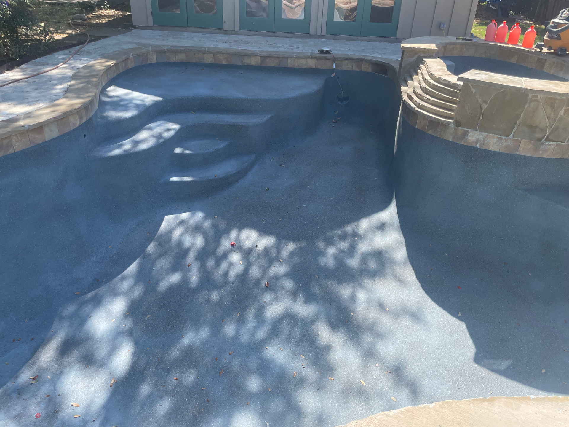 Freshly applied dark pebble finish on freeform pool and spa with travertine coping