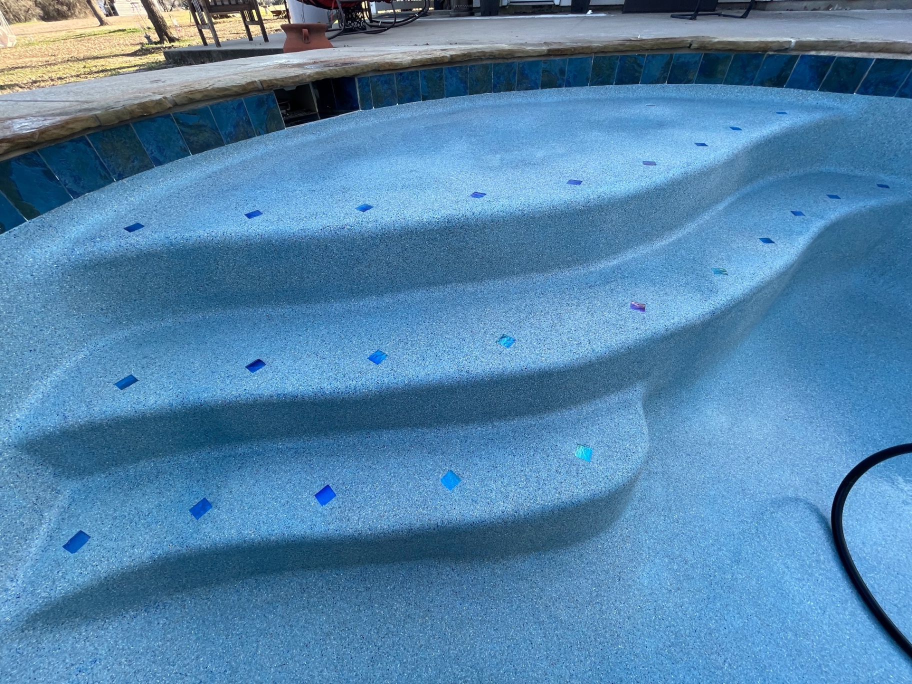 Blue pebble pool steps with iridescent glass tile accents and stained glass waterline tile