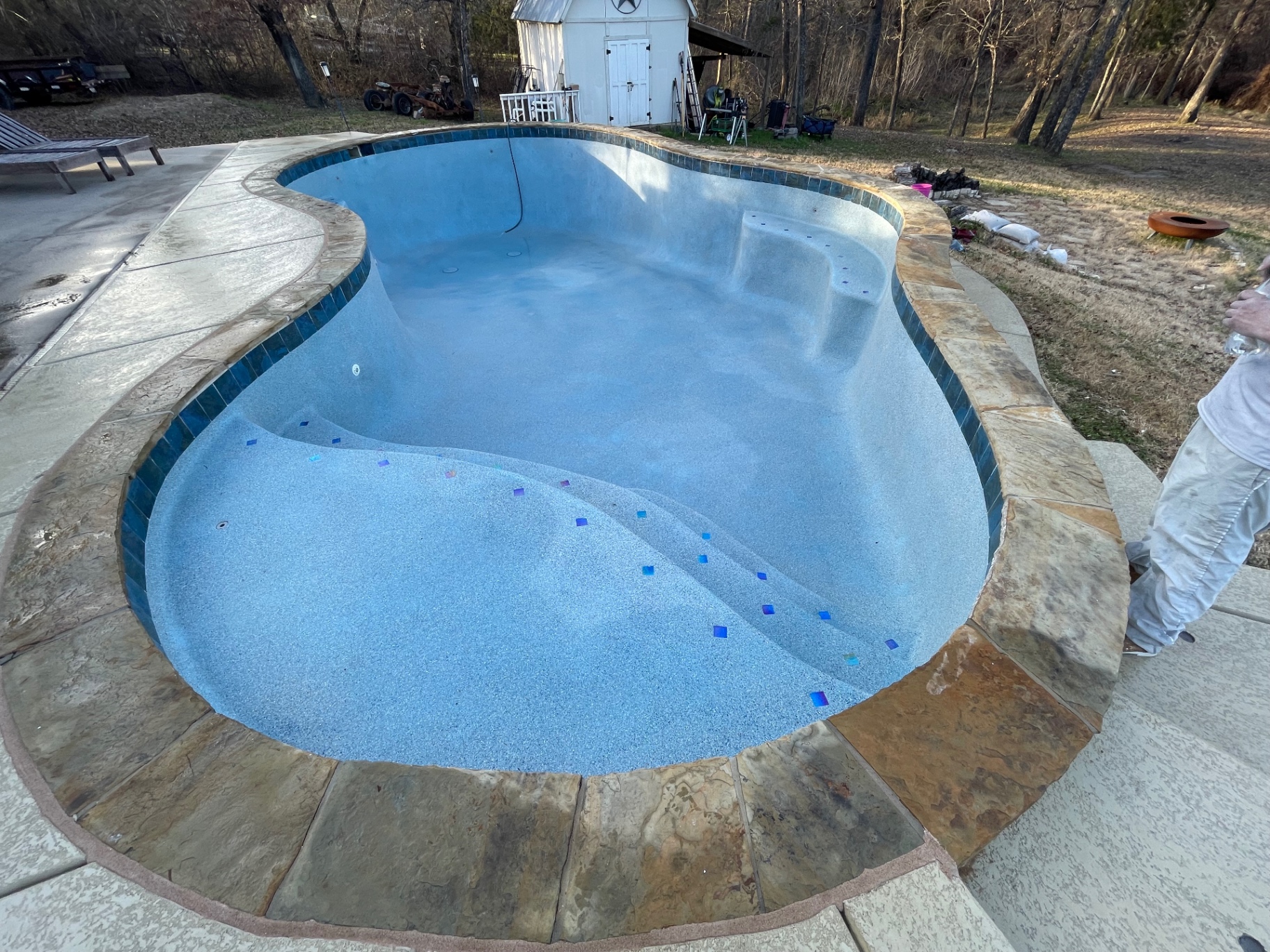 Freeform pool with blue pebble finish, flagstone coping, and glass tile step accents