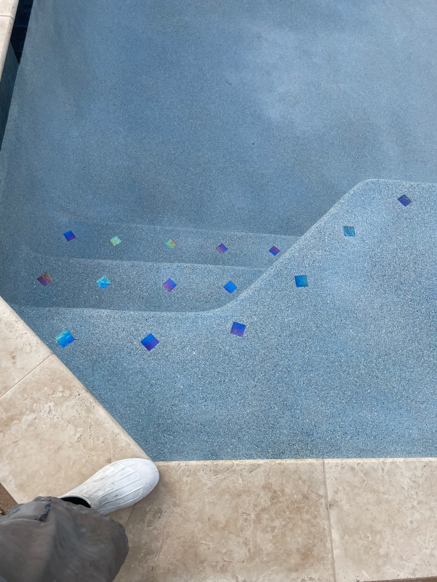 Blue pebble pool steps with iridescent glass tile accents and travertine coping